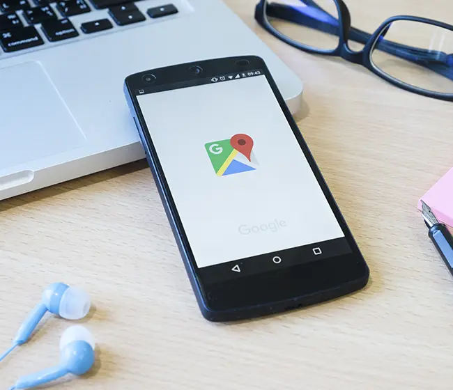 Hvordan optimerer jeg din Google My Business? Telefon der ligger på et bord med høretelfoner, computer og briller.